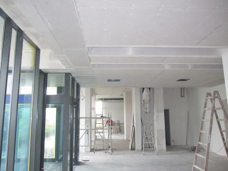 Großer Raum mit Glasfront und fertig beplankter, gelochter Decke; Leitern und Rollgerüst stehen noch