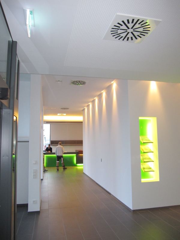 Heller Flur mit Lichtnische, Wandstrahlern und Lüftungsauslass in der gelochten Decke